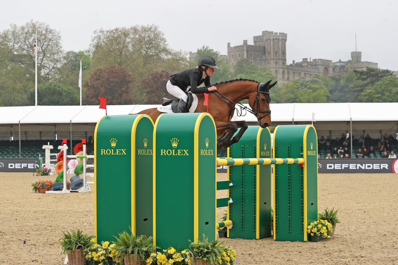 Image of a horse jumping with female trainer looking on
